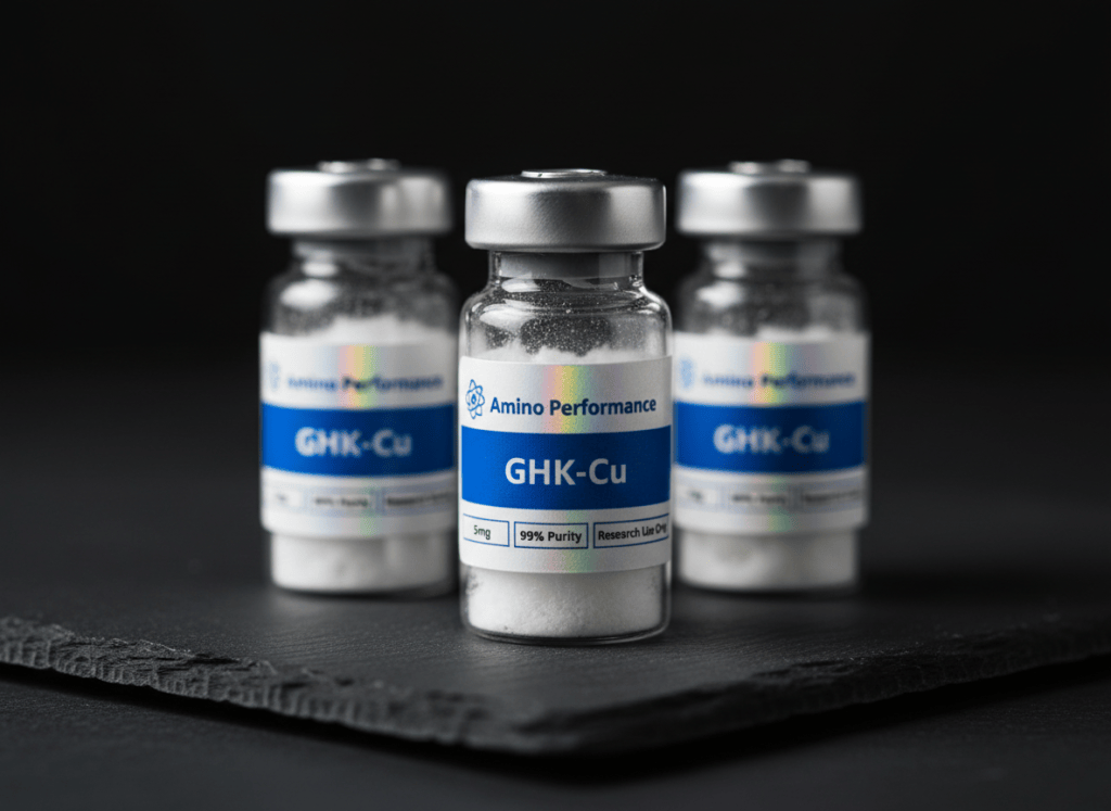 Professional product photography of multiple small glass peptide research vials arranged on a dark near-black surface. Each vial has a holographic iridescent rectangular label wrapped around the body of the vial. The label design exactly matches: holographic/rainbow shimmer background, small blue atom/molecule icon in the top left, "Amino Performance" text in dark ink next to the icon, a solid royal blue rectangular banner in the center of the label with bold white text reading "GHK-Cu", below that on the left a small boxed text "5mg", and on the right "Research Use Only", with "99% Purity" in between. The labels curve realistically around the cylindrical glass vials. The vials are sealed with grey rubber stoppers and aluminium crimp caps. White lyophilized freeze-dried powder is visible inside. Dark moody studio lighting, near-black background, subtle specular highlights on the glass and holographic label shimmer. Premium pharmaceutical research product photography, sharp focus, depth of field.